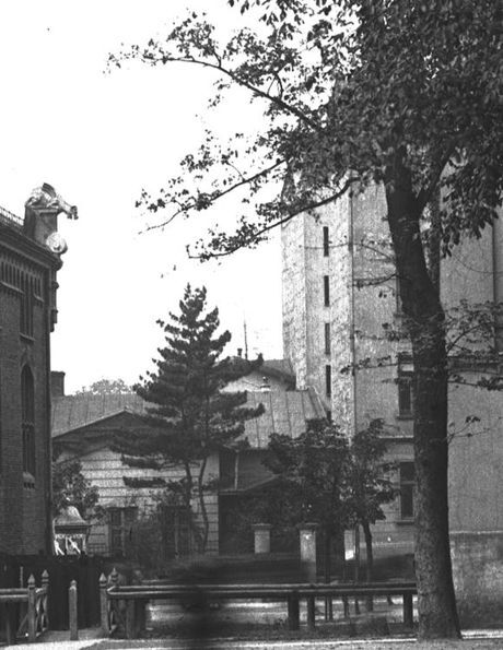 Wycinek fotografii, zbliżenie na fragment kamienicy od strony ul. Biskupiej (widoczna po prawej stronie, za drzewem). 1930 rok.Źródło: Narodowe Archiwum Cyfrowe, sygn. 1-U-2392-3.