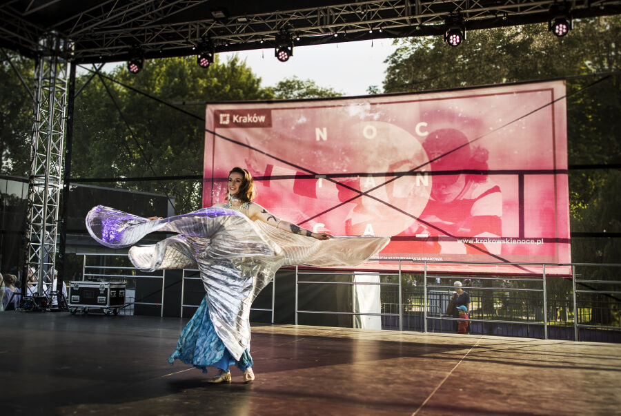 Artystka występuje na scenie w niebieskiej sukience. Na drugim planie wiać banner z Nocą Tańca.