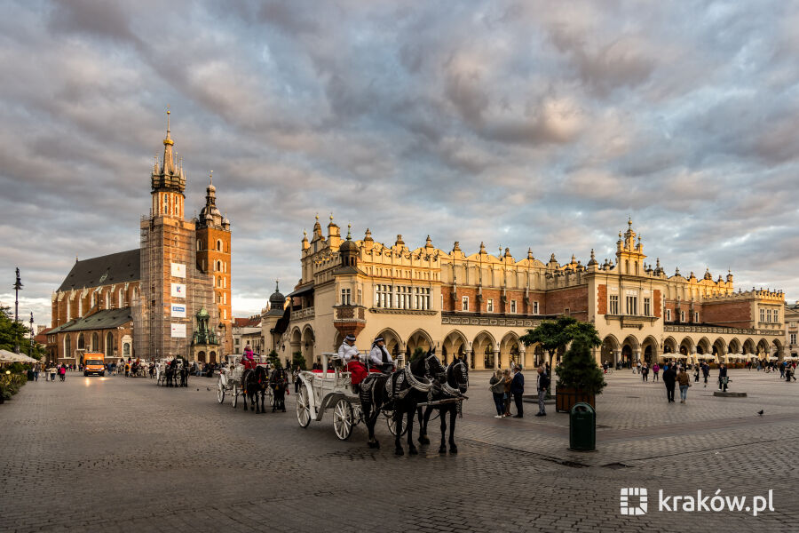 Rynek Główny na którym stoi dorożka w tle sukiennice i kościół mariacki. Niebo z zachodzącym słońcem  