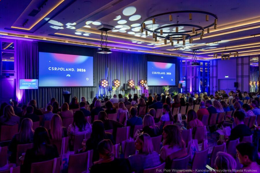 Otwarcie konferencji CSR Poland 2026 w Krakowie 12 marca 2026 r. Na zdjęciu sala konferencyjna z przyciemnionymi światłami i oświetlonym podium na którym stoi moderatorka wydarzenia.                  