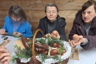 Uczestniczki warsztatów zdobią jajka wielkanocne przy stole, przed nimi stoi kosz ze święconką.
