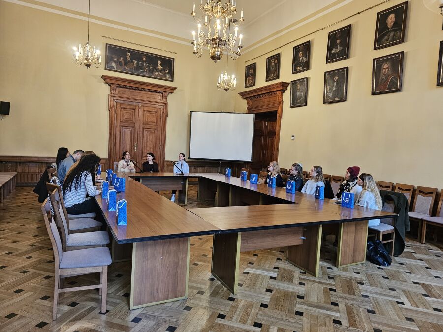 Wizyta studentów socjologii z uniwersytetu w Tilburgu. W przestronnej sali w układzie konferencyjnym siedzi kilkanaście osób.Przy krótszym boku siedzą trzy kobiety i jedna z nich przemawia.   