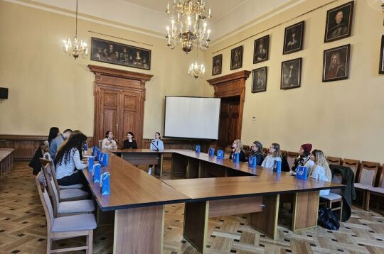 Wizyta studentów socjologii z uniwersytetu w Tilburgu. W przestronnej sali w układzie konferencyjnym siedzi kilkanaście osób.Przy krótszym boku siedzą trzy kobiety i jedna z nich przemawia.   