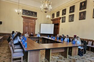 Wizyta studentów socjologii z uniwersytetu w Tilburgu. W przestronnej sali w układzie konferencyjnym siedzi kilkanaście osób.Przy krótszym boku siedzą trzy kobiety i jedna z nich przemawia.   