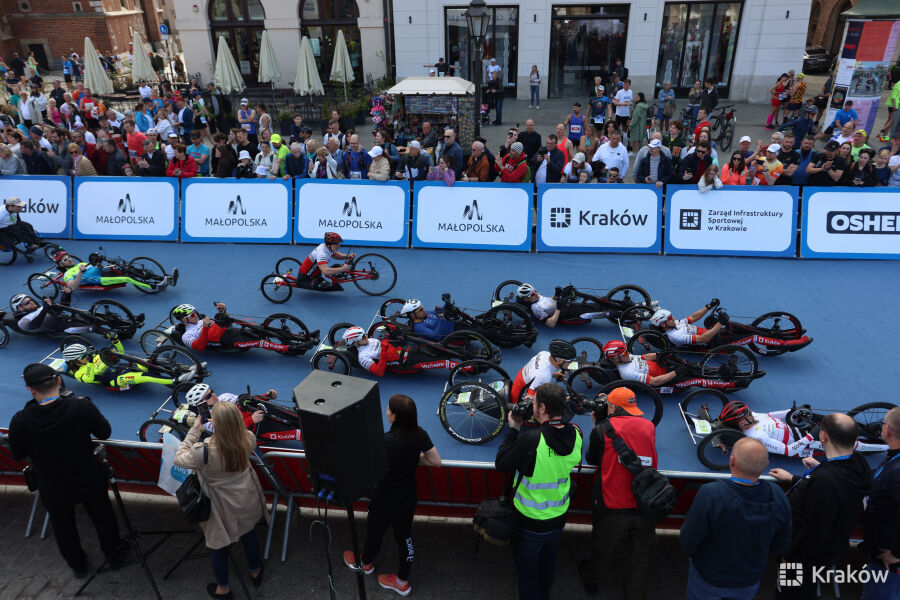 zdjęcie przedstawia maratończyków jeżdżących na wózkach typu hendbajk podczas startu dwudziestego krakowia maraton