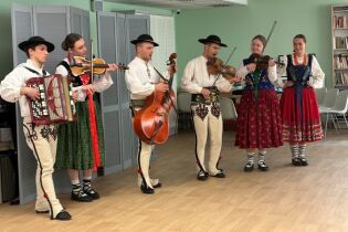 Grupa trzech kobiet i trzech mężczyzn w tradycyjnych strojach góralskich gra na instrumentach ludowych i śpiewa w zamkniętym pomieszczeniu. 