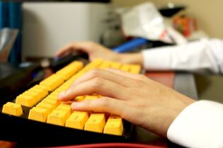 Grafika przedstawia klawiaturę komputerową, na której trzymane są dłonie.
