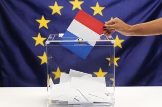 Urna Wyborcza na tle flagi Unii Europejskiej i kobieca ręka trzymająca symboliczna flagę Francji 