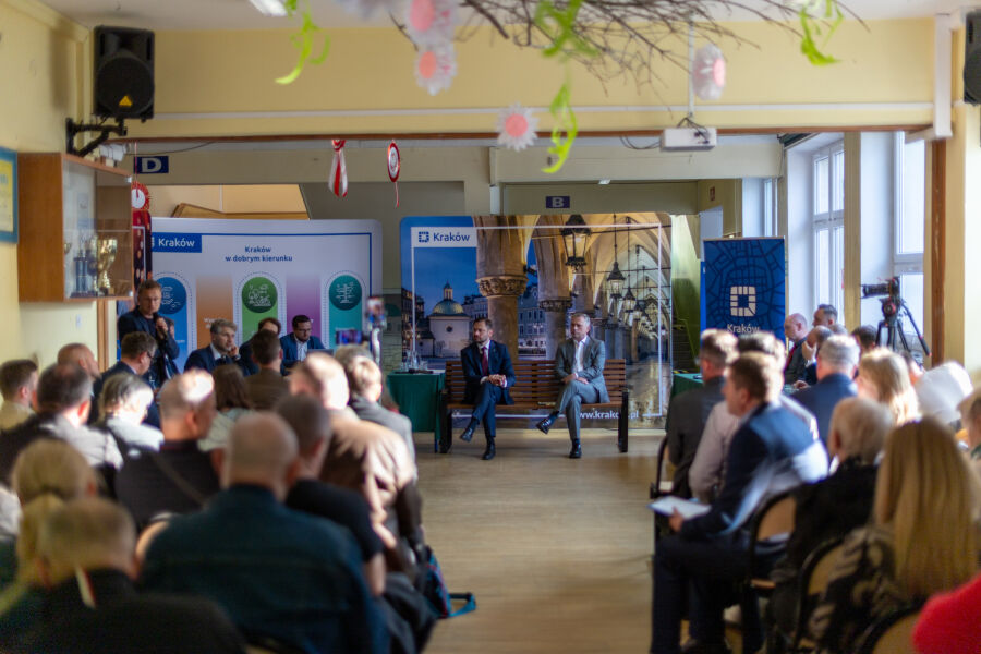 Sala spotkania z uczestnikami widzianymi od tyłu. Na pierwszym planie przedstawiciele miasta biorący udział w „Ławce Dialogu”. W tle widoczne banery informacyjne. Atmosfera formalna, konsultacyjna, w 