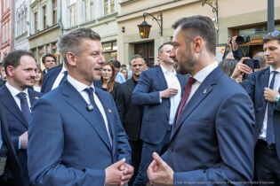 Premier Węgier Peter Magyar i Prezydent Krakowa Aleksander Miszalski rozmawiają stojąc na ulicy Grodzkiej w Krakowie. W tle i po bokach widać mnóstwo przyglądających się osób.  