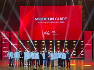 zdjęcie z gala Michelin Guide Polska w Krakowie. na tle dużego czerwonego napisu z nazwą wydarzenia wyświetlanego na potężnych rozmiarów ekranie na scenie stoi kilka osób, mężczyzn i kobiet. 