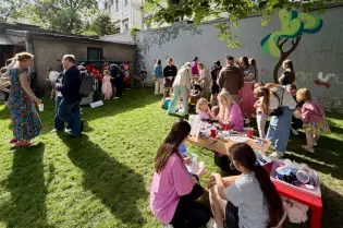 Impreza plenerowa z dziećmi i dorosłymi, stoiska z atrakcjami, mural w tle.