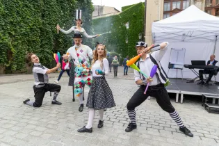 Grupa artystów cyrkowych w kolorowych strojach wykonuje sztuczki na ulicy.