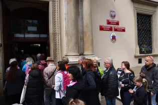 Ludzie stoją w kolejce przed budynkiem urzędowym.