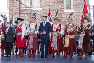 Uroczystość z udziałem mężczyzn w tradycyjnych strojach, z flagami i odznaczeniami.