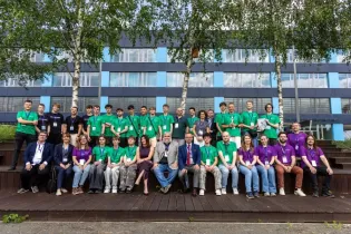 Grupa ludzi w kolorowych koszulkach, pozująca na schodach przed budynkiem.
