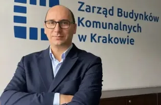 Mężczyzna w garniturze stoi z założonymi rękami przed napisem Zarząd Budynków Komunalnych w Krakowie.
