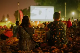 Ludzie oglądający film na dużym ekranie w plenerze, otoczeni przez innych widzów.