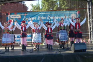 Dzieci w tradycyjnych strojach ludowych tańczą na scenie podczas festiwalu.