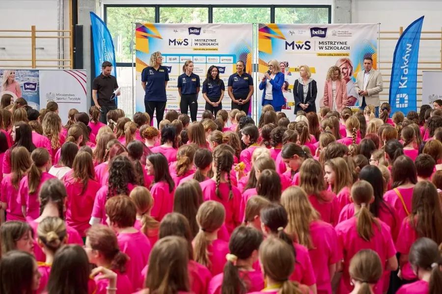 Grupa dzieci w różowych koszulkach podczas wydarzenia sportowego z udziałem trenerów.