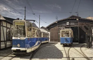 Tramwaje na torach przed zajezdnią, w tle budynek z charakterystycznymi detalami architektonicznymi.