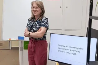 Zdjęcie prowadzącej szkolenie w Centrum Obywatelskim Centrum C 10. Na monitorze napis "Twoje życie i słowa mogą być katalizatorem pozytywnej zmiany w życiu".