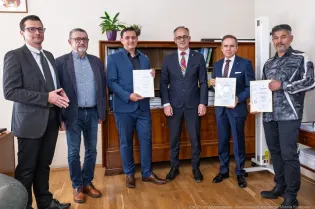 Grupa mężczyzn w garniturach trzymająca dyplomy w biurze.
