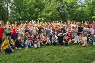 Grupa dzieci i dorosłych pozujących na tle zielonego parku.