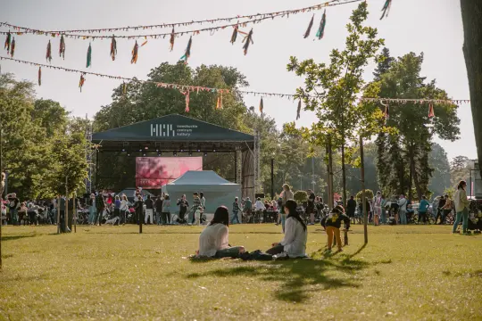 Tłum ludzi na festiwalu w parku, scena z występami, kolorowe dekoracje.