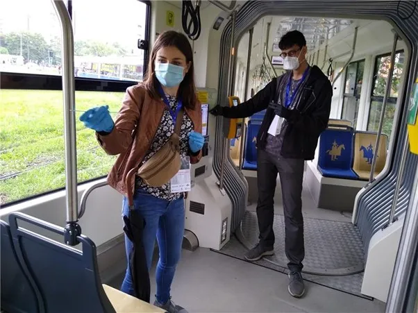 Osoby w maseczkach i rękawiczkach w tramwaju, przygotowujące się do przeprowadzenia testów sanitarnych.