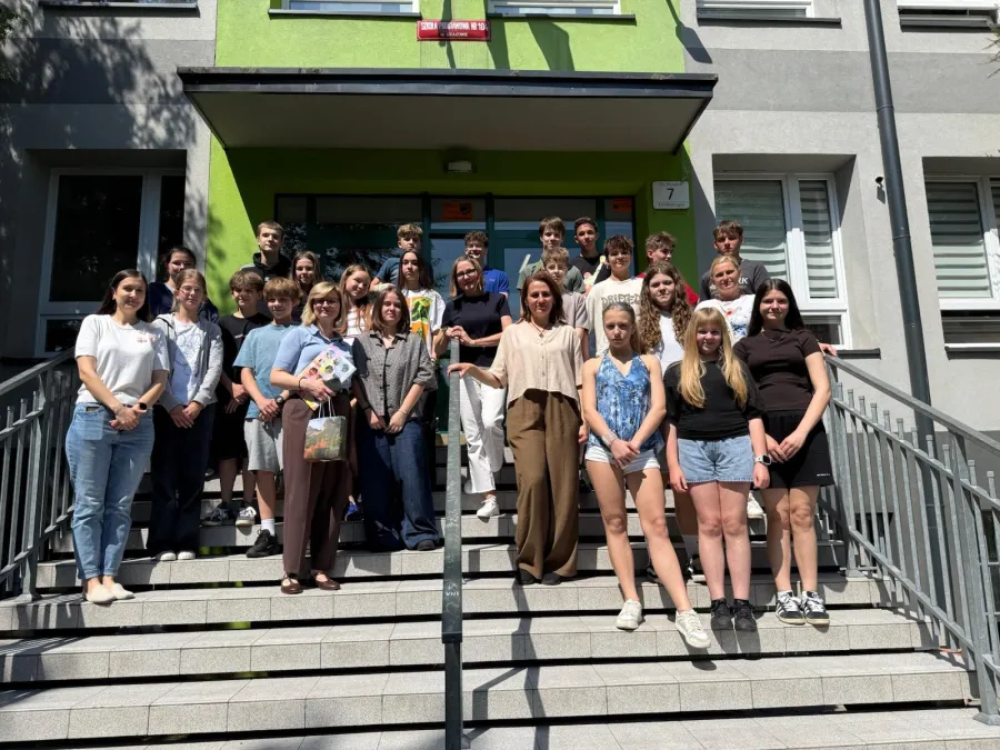 Grupa uczniów i nauczycieli na schodach budynku szkolnego.