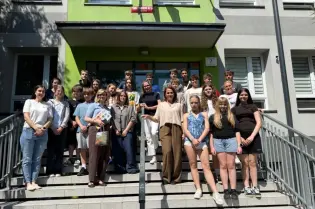 Grupa uczniów i nauczycieli na schodach budynku szkolnego.