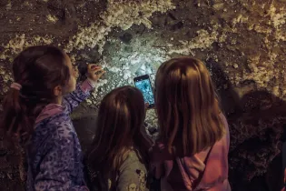 Trzy dziewczynki oglądają ścianę w jaskini, jedna z nich robi zdjęcie telefonem.