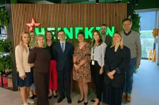 Grupa ludzi stojąca przed zielonym logo Heinekena w biurze.