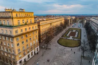 Widok na ulicę z budynkami i parkiem w Warszawie.