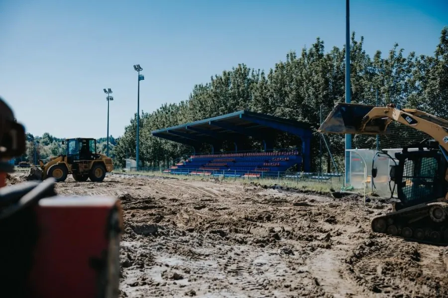 Budowa boiska sportowego z maszynami i widownią w tle.