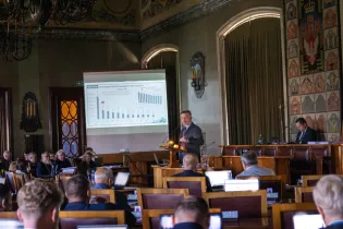 Prezentacja danych w sali obrad z mówcą i uczestnikami przy komputerach.