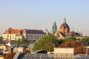 Widok na zabytkowe budynki i kościół w mieście, otoczone drzewa i niebo.