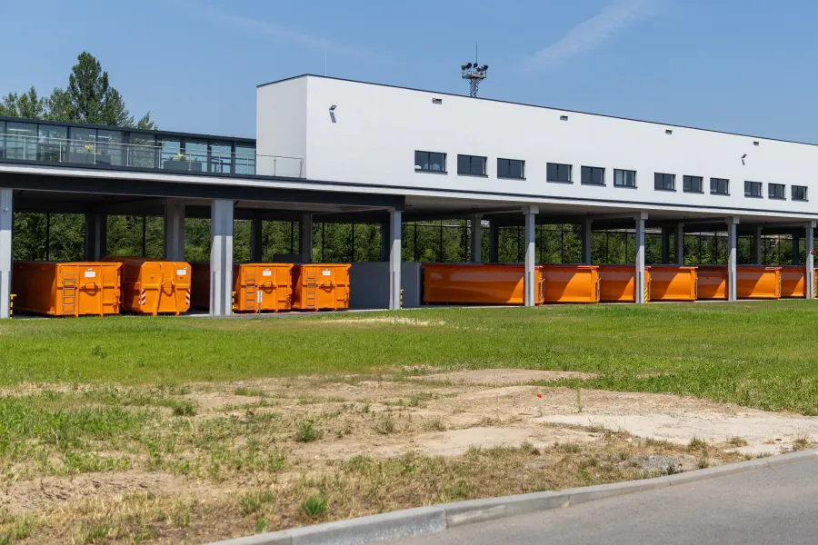 Pomarańczowe kontenery na odpady obok nowoczesnego budynku w słoneczny dzień.