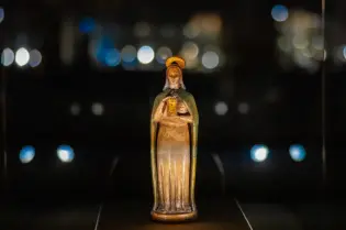Figurka świętej z aureolą, trzymająca księgę, na tle rozmytych świateł.