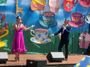 Dwoje artystów występuje na scenie, w tle kolorowe dekoracje z filiżankami i ciastkami.