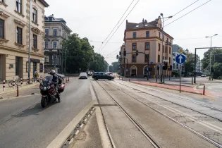 Ruch uliczny z tramwajami, samochodami i motocyklem w miejskim otoczeniu.