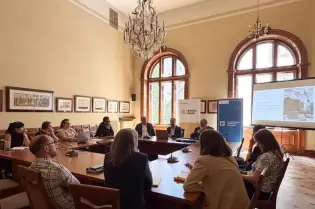Spotkanie w sali konferencyjnej z uczestnikami przy stole i prezentacją na ekranie.
