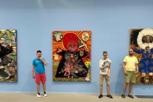 Trzech mężczyzn stoi przed kolorowymi obrazami w galerii sztuki.
