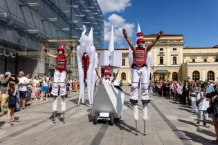 Grupa artystów na szczudłach w kostiumach, prezentujących występ na ulicy.