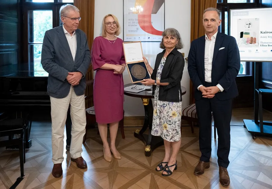 Fotografia wykonana podczas uroczystości wręczenia nagrody im. Karla Dedeciusa w Willi Decjusza 1 lipca 2026 r. Na zdjęciu stoją cztery osoby. Kobieta w środku trzyma otwarte pudełko z medalem.