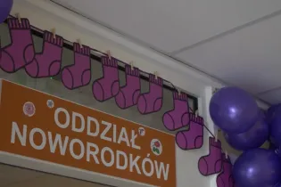 Oddział noworodków z dekoracjami w postaci fioletowych skarpetek i balonów.