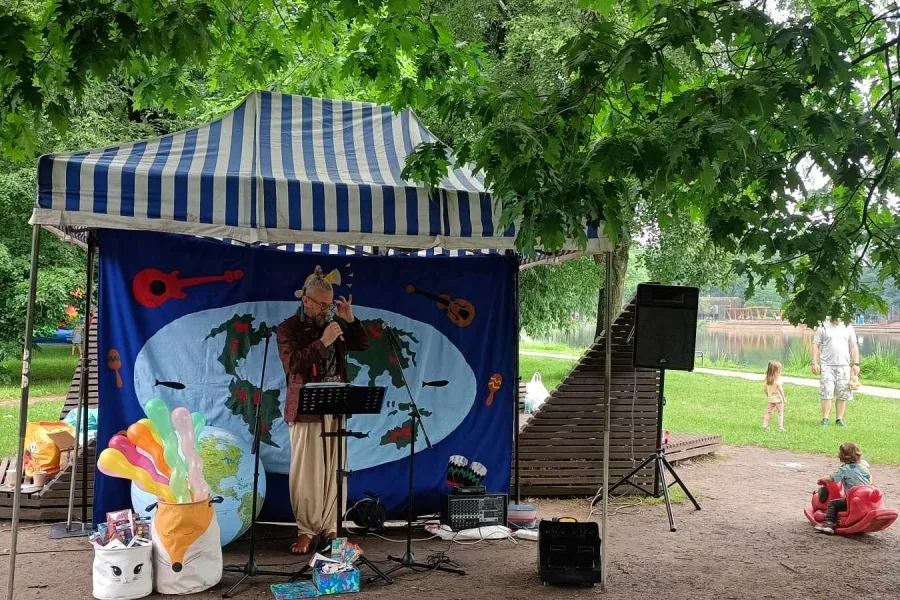 Artysta w kostiumie gra na instrumencie przed dziecięcą publicznością w parku.