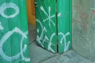 Zielone drzwi z graffiti, częściowo otwarte, prowadzące do wnętrza.
