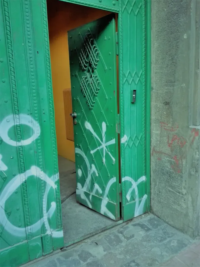 Zielone drzwi z graffiti, częściowo otwarte, prowadzące do wnętrza.